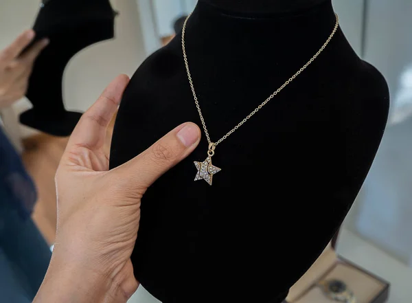 Young woman\'s hand selecting diamond necklace on black hanger in dressing room. At the behide has a blurred image of the reflection in the mirror.