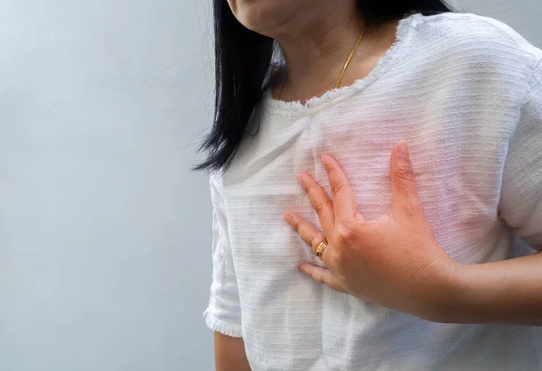 Woman touching chest. Heart attack, heart disease, and chest pain concepts, on light gray background