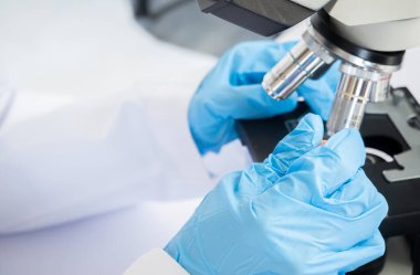 Female cientist hands with genetically modified sample chemicals under a Microscope. Microbiologist working in laboratory with technological equipment.