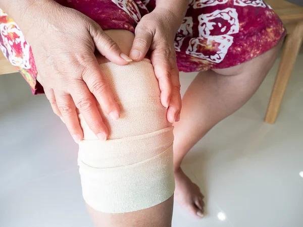 Asian senior or elderly old woman patient with bandage compression knee brace support injury on the wood bench at home.