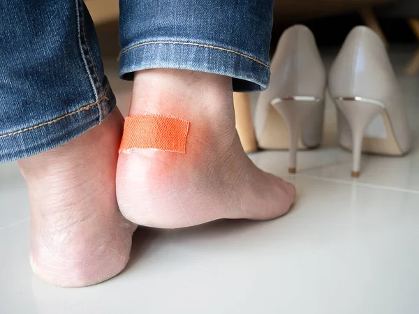 Woman having pain after wearing high heeled tight shoes. Female using bactericidal medical adhesive plaster. Foot skin care, prevention of corns and calluses.