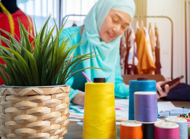 Mutlu gülümseyen Asyalı Müslüman kadın tasarımcı terzi dükkanında çalışıyor. Ev kavramından çalış.