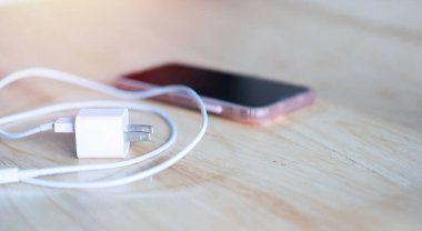 Tahta masada şarj aleti olan akıllı bir telefon. Kablo beyaz ve sarılı..