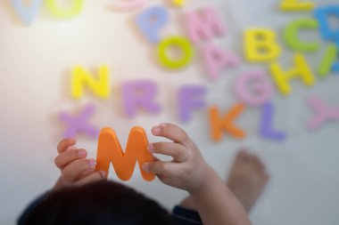 Erkek Asyalı çocuk arka planda çevre dostu alfabe harfleriyle oynuyor. Anaokulu ilköğretim öncesi gelişim kavramı için yazı tipi karakterleri.