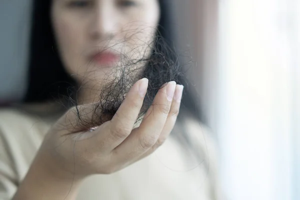Attractive Asian woman serious about her hair  and presentation hair loss problem while looking at many hair in hand.