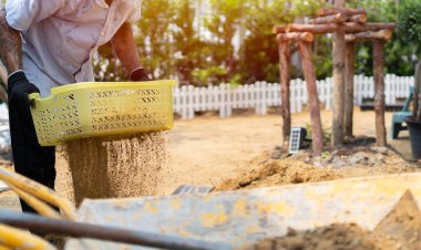 Bahçe aletleri, kürek ve el arabasıyla bir kır evinin sahasında kum yığınıyla çalışmak. İnşaat için hazırlık.