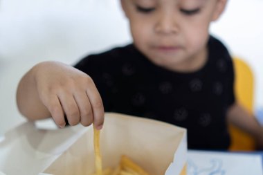 Güneşli bir günde restoranda patates cipsi yiyen küçük Asyalı çocuk masada tek başına otururken sağlıklı beslenme kavramı.