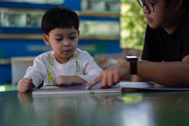 Baba ve oğul kütüphanede birlikte vakit geçirirken bir kitap okuyor ve gülümsüyorlar. Okul öncesi öğrenme kavramı.
