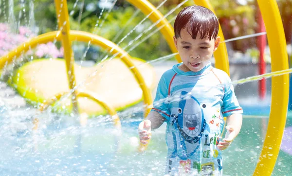 在一个炎热的夏天 快乐的男孩们从公园的喷泉里跑到喷雾器下 孩子们在公园里散步 图库照片