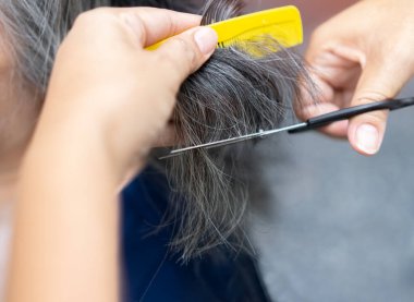 Saç makasıyla çalışan ellerin kesilmiş görüntüsü. Profesyonel kuaför kadın olgun bir kadının saçını kesiyor. Gri saç stili konsepti.
