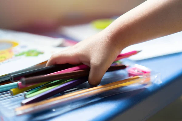 stock image Cropped image of  a little child hand holding a colorful pencils, playing children using pencil crayons  at table indoors. Selective focus. Shot from side.