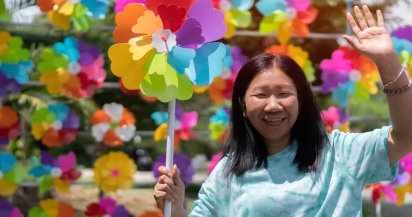 Happy young Asian woman with colorful windmill toy and standing in front of the windmill toy shop. Colorful windmills concept.