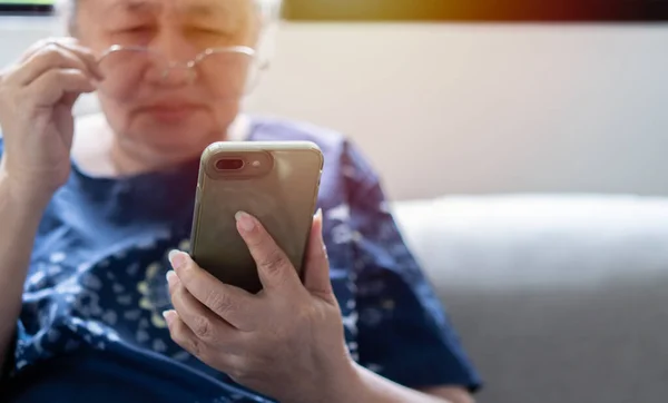 Stock image Asian senior fatigue woman taking off eye glasses during using smartphone after surfing internet or social media at home. Elderly retired male eyesight problem or blurry vision from old aged