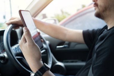 Araba kullanırken cep telefonu tutan genç bir adam mesajları okuyor. Tehlikeli davranış, kaza riski. Tehlike, suç, gençlik, dikkat dağıtma konsepti. Eline odaklan..
