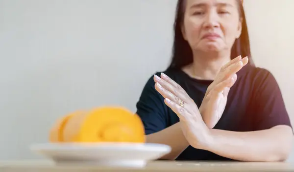 Sad Asian woman not allowed to eat sweet foods and suffering from a toothache, she is not allowed to take sweet foods. Dental problem concept, selective focus at hands.