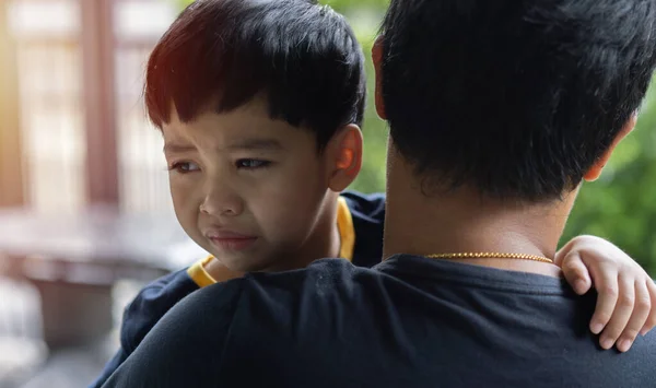 Close up sad young Asian boy crying on father hands in nature park outdoor. Man holds son, hugs and comforts. Family love, care and moral support, baby tears, daddy\'s arms. Dad consoling crying child