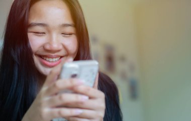 Gülümseyen Asyalı kız cep telefonu uygulaması kullanıyor, oyun oynuyor, internetten alışveriş yapıyor. Ev konseptinde akıllı telefon kullanmak.