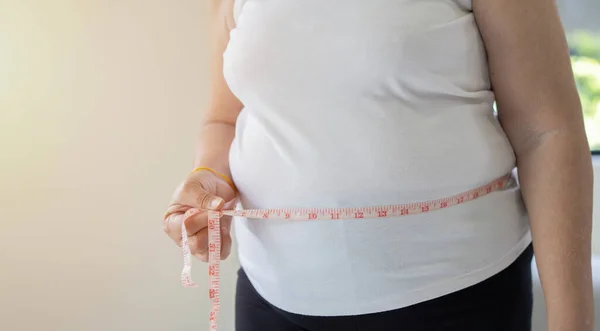 胖胖的女人的手用测量带测量她的腰围 健康概念和体重减轻 — 图库照片