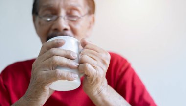 Emekli yaşlı bir adamın kırmızı tişört giydiği ve evde dinlenirken elinde bir fincan kahve tuttuğu fotoğraf. Emekli yaşam tarzı konsepti. Ellere seçici odaklanma.