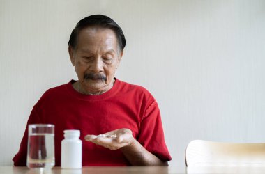 Reçeteli ilaç. Bir bardak su ve şişe yanında dururken yaşlı bir erkeğin elindeki haplara baktığı seçmeli bir odak noktası..