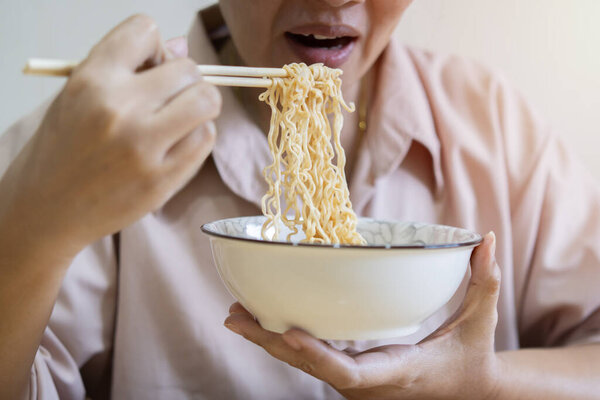 Cropped image of  woman isolated on beige background holding a bowl of noodles with chopsticks and eating it. Close up and selective focus at noodles.