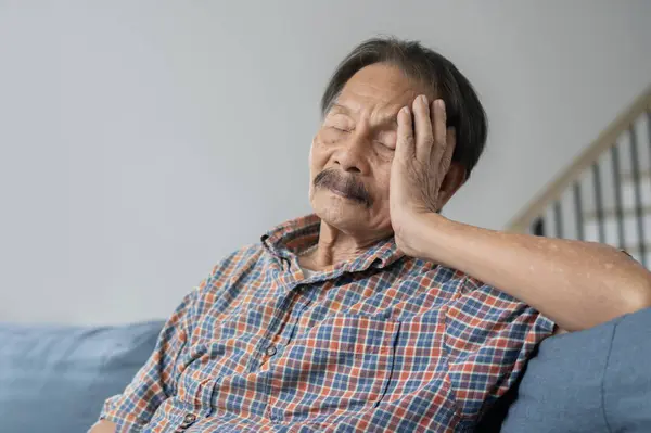 Tired elderly Asian man relax fall asleep on comfortable couch in living room, exhausted mature male take nap daydreaming on cozy sofa at home.