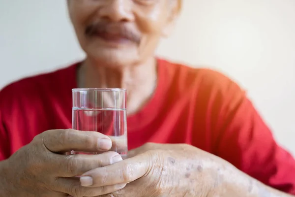 A glass of water in the wrinkled hands of an elderly man, grandfather drinks water, health care, the benefits of drinking water for an old man.