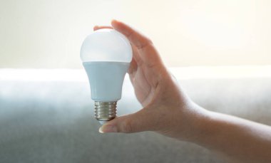 Fotokopi alanı olan gri arka planda LED ampulü tutan kadın. Yaratıcı fikir, yeni iş planı, motivasyon, yenilik, ilham kavramı