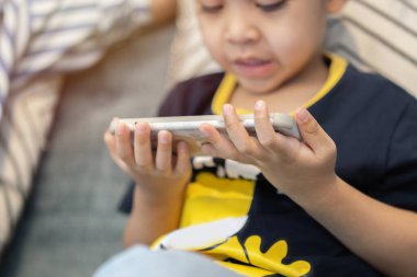 Koyu mavi tişörtlü küçük bir çocuk bilgisayar oyunları için akıllı telefondan yarış uygulaması kullanıyor. Eldeki seçici odaklanma.