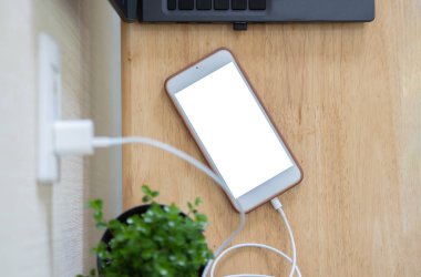 Elektrikli şarj aletini ahşap masadaki boş ekranla cep telefonuna bağlamaya hazırız. Güç tasarrufu ya da maliyet azaltma kavramı. Üst görünüm