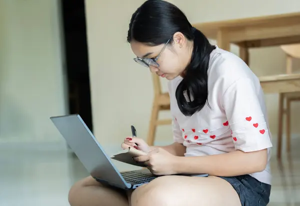 Note Taking. Side view portrait of female student using laptop and writing memo in her diary at home. Online education, elearning concept