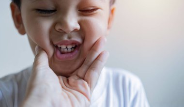 Anne, bebeğin ilk dişlerini muayene etmek için ellerini açar. Neşeli çocuk diş fırçalarını gösteriyor. Küçük çocuk diş temizliyor..
