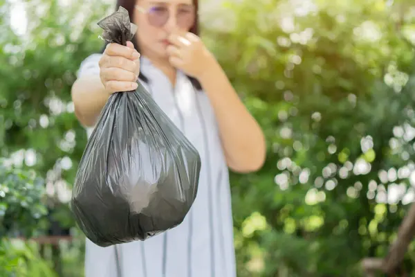 Recycling, sorting and sustainability concept - young Asian woman holding stinky trash plastic bag over garden background.