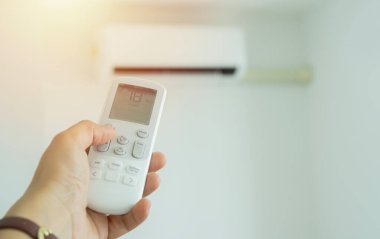 Odanın içinde kadın uzaktan kumandalı bir klima var. - Uzaktan kumandalı klima. Eldeki seçici odaklanma.