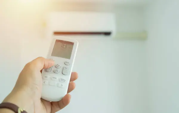 Air conditioner inside the room with woman operating remote controller. / Air conditioner with remote controller. Selective focus on hand.