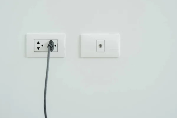 White electrical plug in the electric double socket and cabel socket on white wall. Selective focus, copy space.