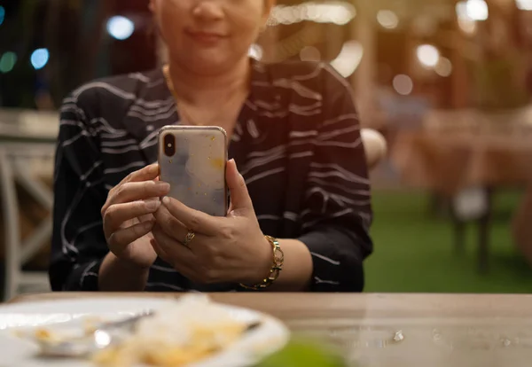 Excited lady using smartphone in restaurant while having dinner, sitting at table and texting on phone, browsing social networks or shopping online, free space