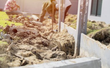 İşçilerin hafif odak noktası, inşaat alanındaki direğin etrafında kürek ve toprak kazıyor. Toprak kazma kavramı.