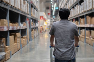 Depodaki rafların arasında duran alışveriş arabalı Asyalı sakallı yetişkin bir adamın arkası. Seçici odak.