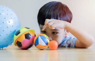 Sevimli şirin çocuk eğlenceli ve mutluluk dolu renkli toplar oynuyor, neşeli gülüyor, hafta sonu tatilinde evde oturma odasında gülümsüyor. Çocuklar ve Eğitim Konsepti