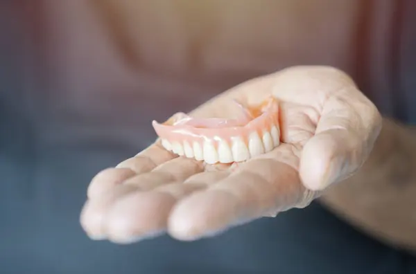 An elderly man holds a denture. A man is holding dentures in his hand. Removable dentures flexible.