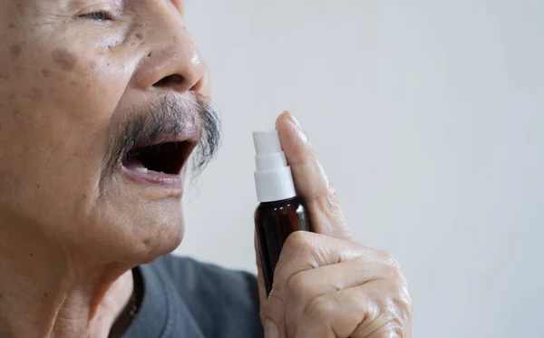 Spray for sore throat. Photo of a old man who treats her throat with a spray and sprinkles it in his mouth. The concept of health and disease.