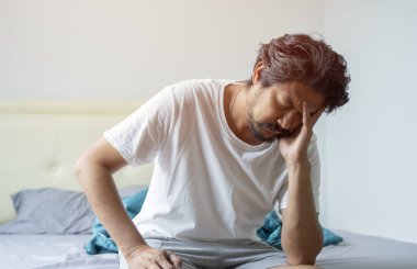 Uykusuzluk, uyku bozukluğu konsepti. Uykusuz, mutsuz, gri saçlı, pijama giyen orta yaşlı bir adam evde oturuyor, kafasına dokunuyor.