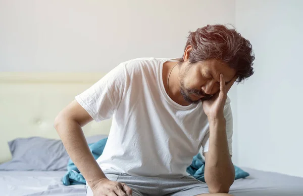 Uykusuzluk, uyku bozukluğu konsepti. Uykusuz, mutsuz, gri saçlı, pijama giyen orta yaşlı bir adam evde oturuyor, kafasına dokunuyor.