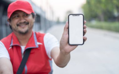 Asyalı mutlu bir teslimatçı bisikletin üzerinde oturuyor ve boş ekranlı akıllı telefonu gösteriyor. Telefona seçici odaklanma.