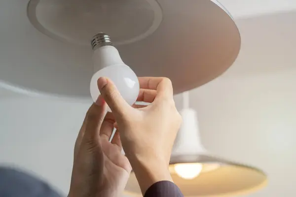 Cropped image of woman hands changing light bulb in hanging lamp at home. Moving, electricity and repair concept