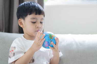 Elinde dünyayı tutan bir çocuğun kavramsal fotoğrafçılığı. Asyalı küçük çocuk kanepede oturup evdeki pencereden gerçek güneş ışığıyla top oynuyor..