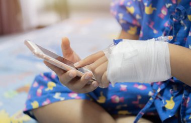 Küçük çocuk hastane yatağında damardan sıvı tedavisi görüyor. Hasta bebek cep telefonu kullanıyor. Seçici odak.