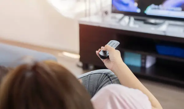 Kanepede dinlenen bir kadın uzaktan kumandayı kullanıyor ve televizyon menüsünden bir televizyon dizisi ya da film seçiyor. Arka plan, seçici odak.