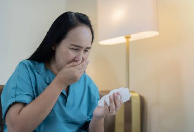Asyalı bir kadının yan görüş portresi, evde oturup akciğer kanserini riske atan zatürree öksürüğünden endişelenmek, tükürüğünde kan görmek onu şok etti..
